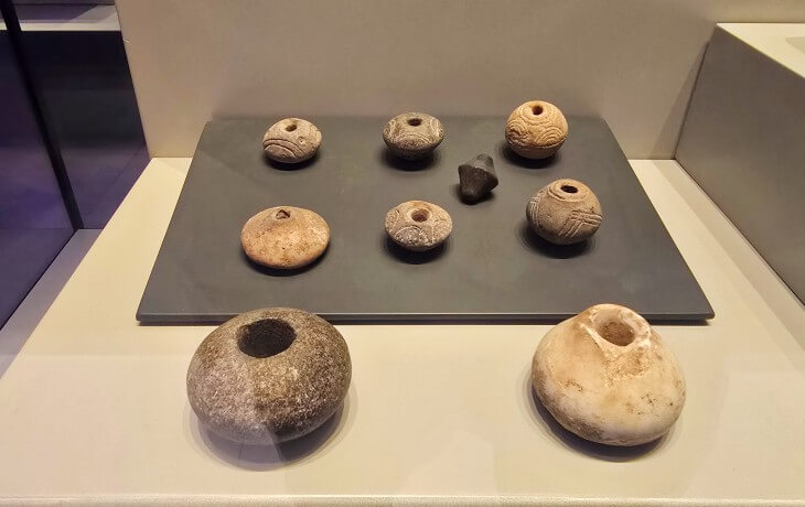 İznik Müzesi’nde sergilenen taş boncuklar, delikli taş ağırlıklar ve geometrik bezemeli küçük taş objelerin vitrindeki detaylı düzenlemesi.